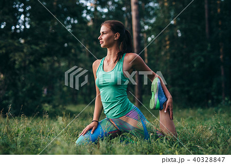 Young sportswoman warming-up before workout doing stretching exercises sitting on grass in park 40328847