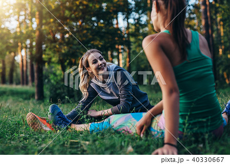 Two cheerful female athletes warming up before training doing stretching exercise for legs sitting Two cheerful female athletes warming up before training doing stretching exercise for legs sitting 40330667