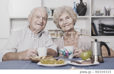 Smiling elderly spouses enjoying tea with sweets 40334315