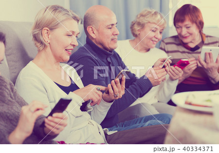 Mature friends are resting together and looking at their phones Mature friends are resting together and looking at their phones 40334371