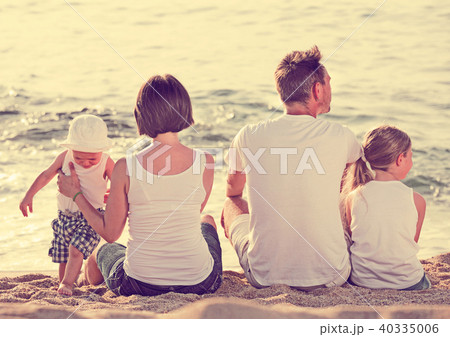 Man and woman with kids sitting with back to camera on beach 40335006