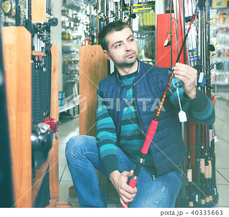 engrossed male choosing fishing rod for fishing in the sports shop engrossed male choosing fishing rod for fishing in the sports shop 40335663
