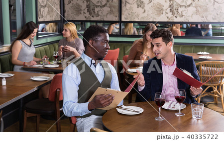 Сheerful male friends choosing dishes from menu card in restaurant Сheerful male friends choosing dishes from menu card in restaurant 40335722