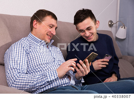 Adult male with his son are resting together and playing on phone 40338007