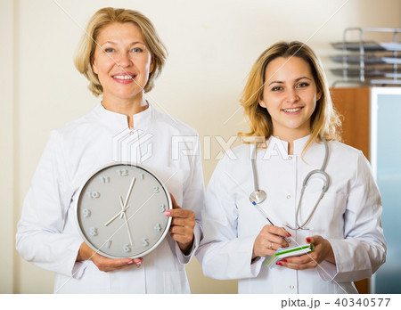 Two friendly doctors holding clock and smiling in modern clinic 40340577