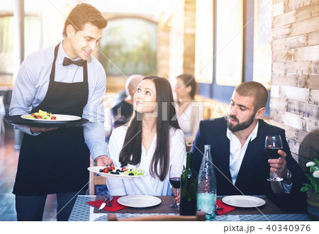 Waiter with dishes serving man and woman friendly company indoors 40340976