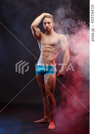 Strong athletic young man with huge muscles posing over smoke ba 40359410