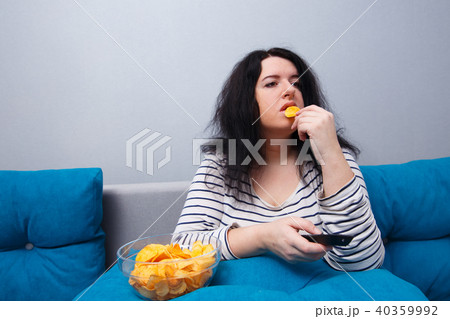 Fat overweight woman sitting on the sofa, eating chips while wat 40359992