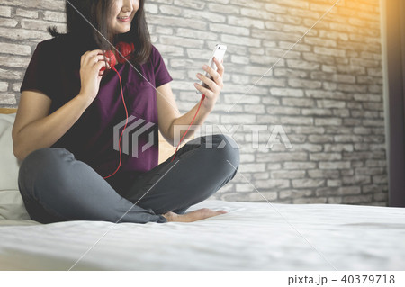 Young woman sitting in her bed and listening music in her bedroo 40379718