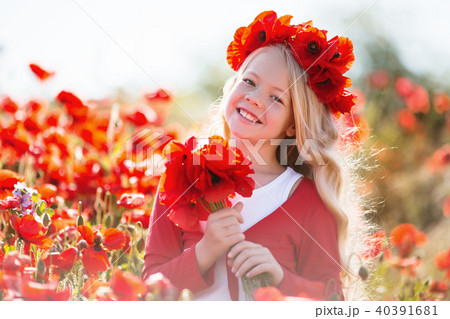 Cute smiling blonde child girl is wearing wreath from red flowers in poppy field 40391681