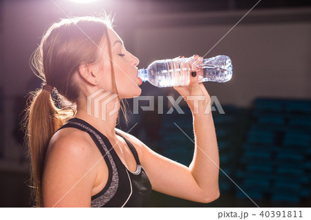 Fitness young woman drinking water in the gym. Muscular woman taking break after exercise 40391811