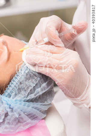 Close up of hands of young cosmetologist injecting in female face Close up of hands of young cosmetologist injecting in female face 40393817