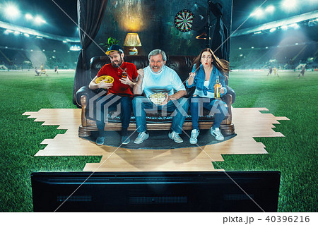 Ardent fans are sitting on the sofa and watching TV in the middle of a football field. Ardent fans are sitting on the sofa and watching TV in the middle of a football field. 40396216
