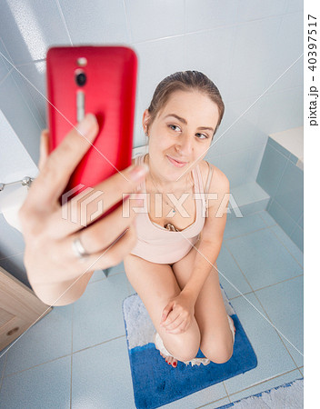 Closeup image of young woman sitting on toilet and making selfie on mobile phone 40397517