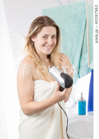 Portrait of young blonde woman drying hair with hairddryer and looking in camera Portrait of young blonde woman drying hair with hairddryer and looking in camera 40397963