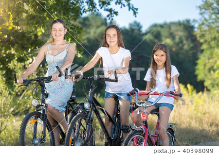 Portrait of two teenage girls riding bicycles with mother in park 40398099
