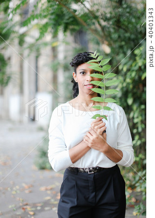 Stylish black girl standing with green leaf and wearing white blouse and having bangs. 40401343