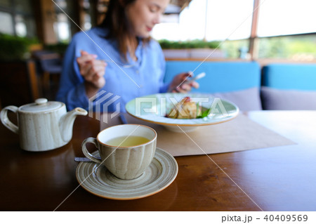 Close up cup of tea, kettle and female person eating dessert in background at cafe, using smartphone Close up cup of tea, kettle and female person eating dessert in background at cafe, using smartphone 40409569