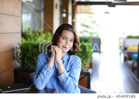 Pretty woman sitting at cafe leaning on hand, wearing jeans shirt Pretty woman sitting at cafe leaning on hand, wearing jeans shirt 40409586
