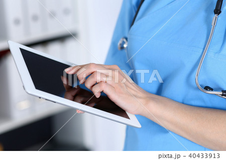 Woman doctor using tablet computer while standing straight in hospital office, closeup. Healthcare 40433913