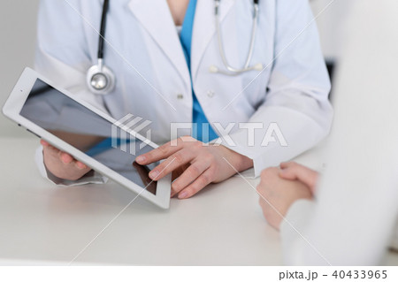 Closeup of a doctor and  patient  sitting at the desk. Physician pointing into tablet pc. Medici 40433965
