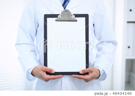 Unknown male doctor standing straight while holding medical clipboard with blank white paper Unknown male doctor standing straight while holding medical clipboard with blank white paper 40434140
