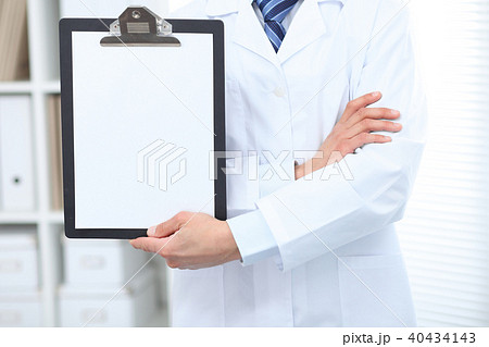Unknown male doctor standing straight while holding medical clipboard with blank white paper Unknown male doctor standing straight while holding medical clipboard with blank white paper 40434143
