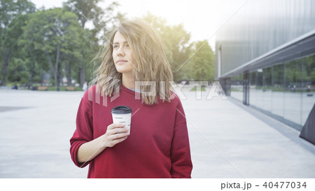 A young cute casual brunette girl is drinking coffee outside in the morning A young cute casual brunette girl is drinking coffee outside in the morning 40477034