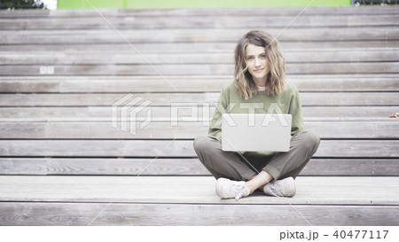 A young girl is working in a park with a laptop sitting on the stairs A young girl is working in a park with a laptop sitting on the stairs 40477117