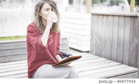 A young cute girl sitting in the park drinking coffee with a tablet 40477434