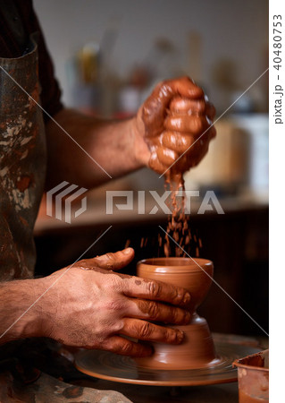 Close-up hands of a male potter in apron making a vase from clay, selective focus Close-up hands of a male potter in apron making a vase from clay, selective focus 40480753