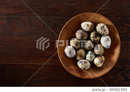 Fresh quail eggs in a wooden plate on a dark wooden background, top view, close-up Fresh quail eggs in a wooden plate on a dark wooden background, top view, close-up 40482309