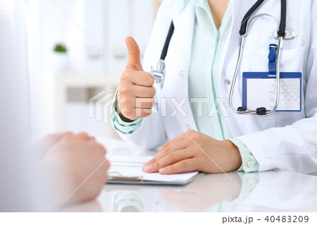 Doctor showing Ok sign and thumb up to patient while sitting at the desk in hospital office, closeu Doctor showing Ok sign and thumb up to patient while sitting at the desk in hospital office, closeu 40483209