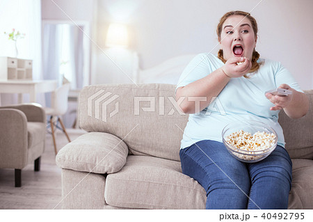 Dreamy red-head woman eating popcorn on the couch 40492795