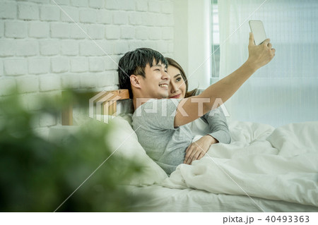 Happy Asian Lover sitting and using the digital smart mobile phone to selfie on the bed of bedroom at modern home, Couple successfull and lifestyle concept 40493363