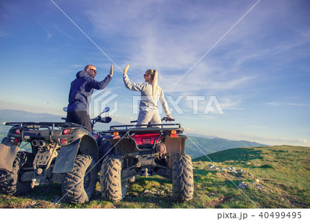 Rear view of young pair near atv. Man is showing something in distance to her girlfriend. 40499495