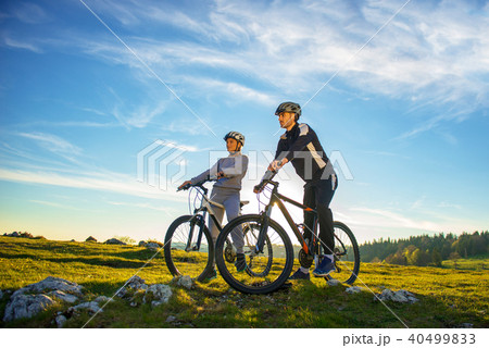 Cyclist couple with mountain bikes standing on the hill under the evening sky and enjoying bright 40499833