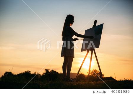Silhouette of a blonde girl paints a painting on the canvas with the help of paints. A wooden easel 40501986