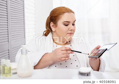 Concentrated plump woman applying make-up 40508091