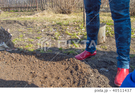 Women's fit in jeans and red rubber boots, a woman farmer stands in his garden prepares the ground Women's fit in jeans and red rubber boots, a woman farmer stands in his garden prepares the ground 40511437