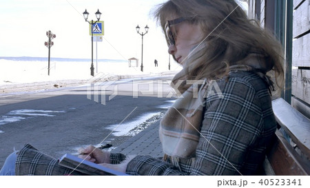 young, beautiful, lovely woman sitting on bench in park, in hands of her notebook. She is wearing a 40523341
