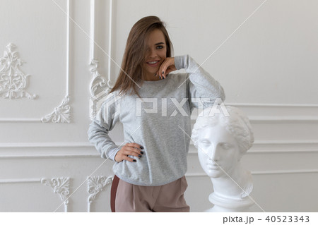 A smiling young woman in a gray sweetshot stands near a white statue. 40523343