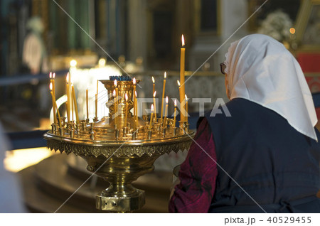An old woman puts a candle in front of an icon An old woman puts a candle in front of an icon 40529455