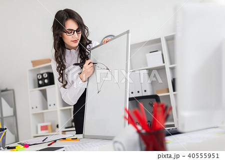 A beautiful young girl stands near an office desk and draws a magnetic marker on the magnetic board. A beautiful young girl stands near an office desk and draws a magnetic marker on the magnetic board. 40555951