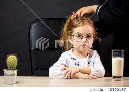 Gloomy little girl in spectacles refusing to drink milk, over black backgrounf 40560137