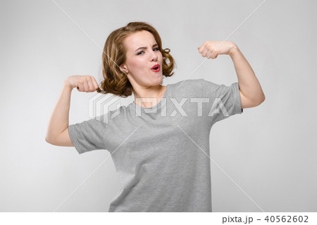 Charming young girl in a gray T-shirt on a gray background. Girl showing muscles 40562602