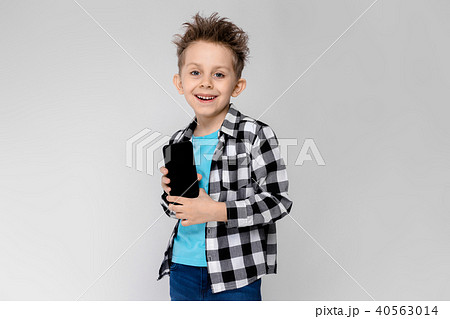 A handsome boy in a plaid shirt, blue shirt and jeans stands on a gray background. The boy is 40563014