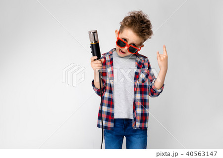 A handsome boy in a plaid shirt, gray shirt and jeans stands on a gray background. A boy wearing A handsome boy in a plaid shirt, gray shirt and jeans stands on a gray background. A boy wearing 40563147