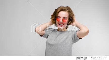 Charming young girl in a gray T-shirt on a gray background. Happy girl in red glasses Charming young girl in a gray T-shirt on a gray background. Happy girl in red glasses 40563922