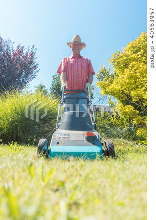 Active senior man smiling while using a grass cutting machine in the garden Active senior man smiling while using a grass cutting machine in the garden 40563957